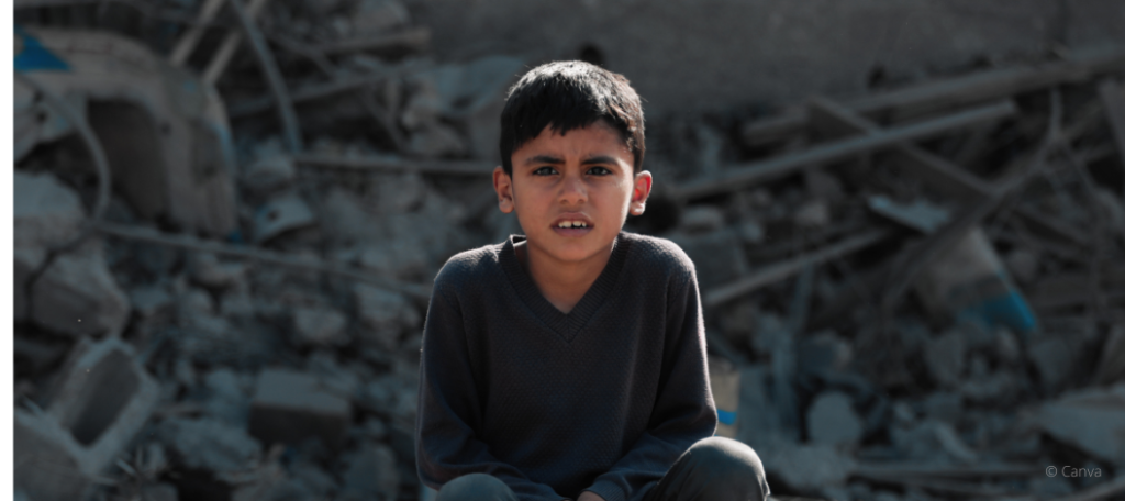 Ein Junge sitzt mit ernstem Blick vor zerstörten Gebäudetrümmern, Symbol für die Not und Unsicherheit in Krisengebieten