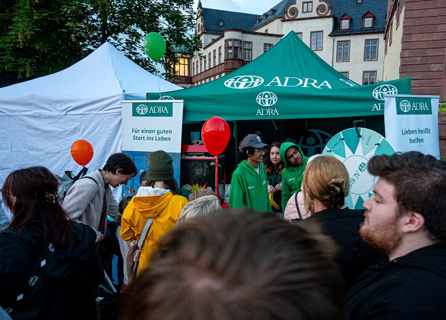 Der grüne ADRA-Pavillon auf dem Schlossgrabenfest in Darmstadt mit Informationsbannern. Zahlreiche Menschen stehen davor und informieren sich.