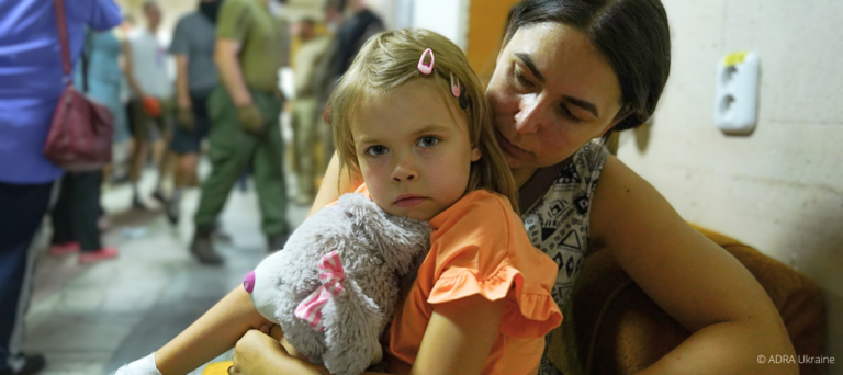 ADRA leistet Nothilfe nach Bombenangriff auf Kinderkrankenhaus in Kiew: Eine Mutter hält ihre Tochter mit Kuscheltier im Arm – Angst und Erschöpfung sind ihnen ins Gesicht geschrieben.