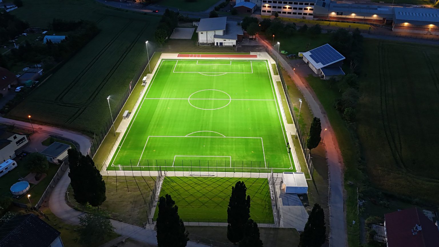 Neuer Kunstrasenplatz abends beleuchtet durch Flutlichtanlage, mit Blick auf das neue Kleinspielfeld. Drohnenaufnahme vom RSV Arloff-Kirspenich e.V.