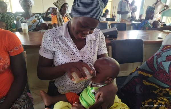 Eine Mutter aus Burkina Faso versorgt ihr Baby mit notwendiger Babynahrung als Teil der nachhaltigen Landwirtschaftsinitiativen von ADRA zur Bekämpfung von Unterernährung