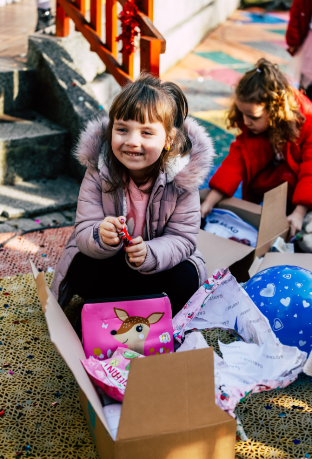 Mädchen aus Osteuropa öffnet Weihnachtspäckchen und freut sich über Geschenke aus der Aktion „Kinder helfen Kindern!“