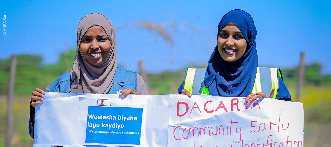 Zwei Frauen aus Somalia halten einen Banner hoch und präsentieren ihn in die Kamera – Symbol für gemeinschaftliche Aktion und Katastrophenvorsorge.