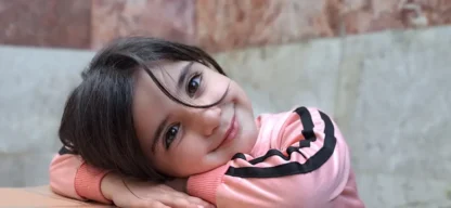 MehrAlsEinWunsch -Junges Mädchen aus Syrien lächelt und legt den Kopf auf ein ADRA-Paket.