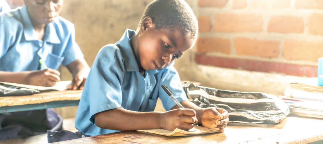 Ein Kind sitzt in einem Klassenraum an einem Schreibtisch und schreibt konzentriert in ein Heft. Das Bild verdeutlicht, wie Spenden für Bildung einem Kind die Chance geben, ein Schuljahr mit Schulgebühren, Uniform und Lehrmaterial abzuschließen.