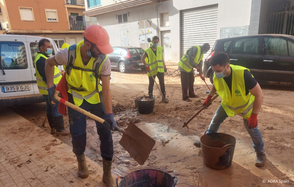ADRA-Helfer räumen mit Schaufeln Schlamm und Trümmer von den Straßen in einer von der Flut betroffenen Stadt in Valencia.