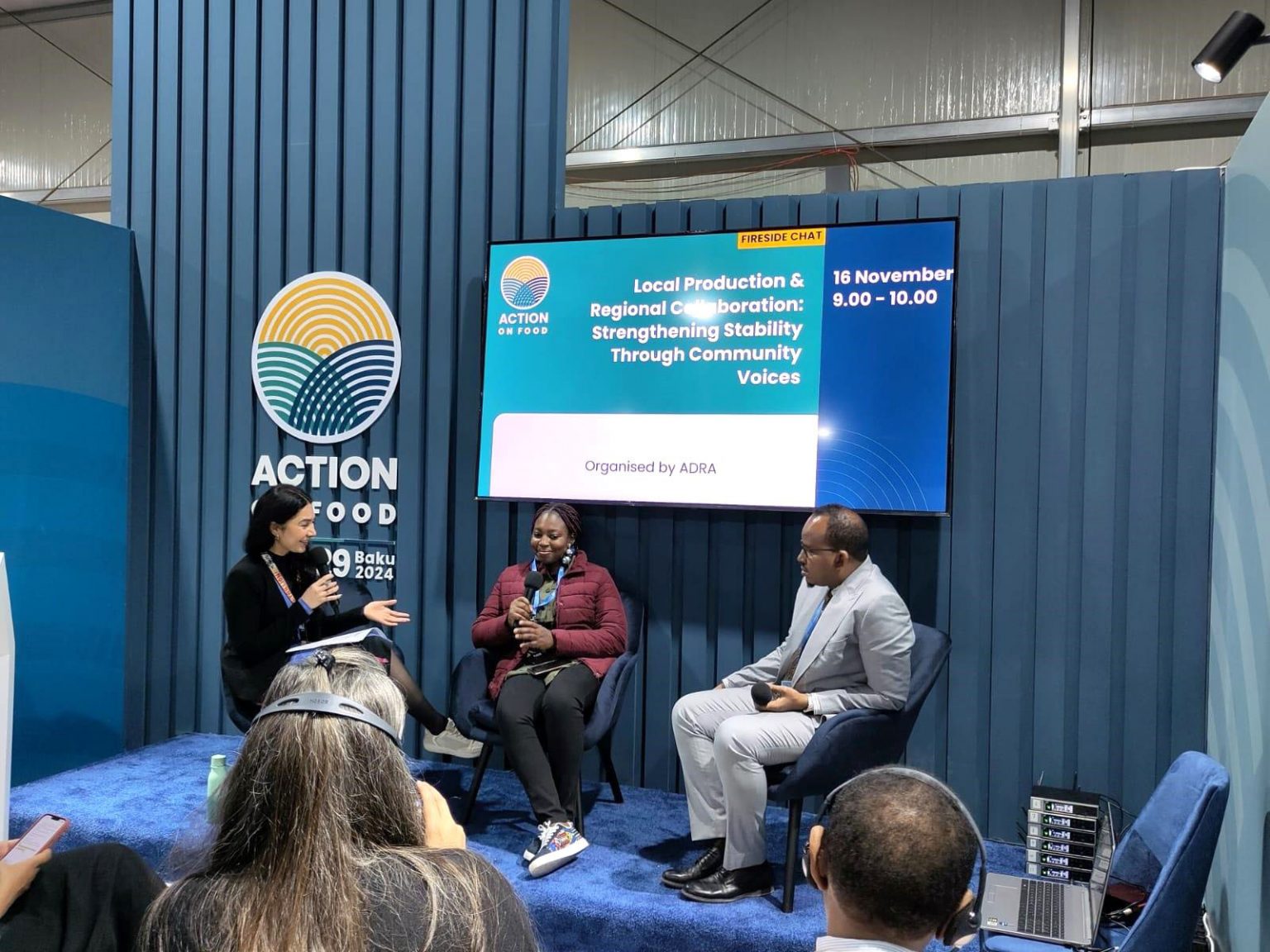 Carina Rolly, ADRA-Referentin, spricht auf der COP29 in Baku vor großem Publikum, mit zwei weiteren Personen auf der Bühne