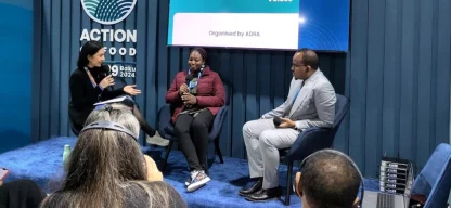 Carina Rolly, ADRA-Referentin, spricht auf der COP29 in Baku vor großem Publikum, mit zwei weiteren Personen auf der Bühne.