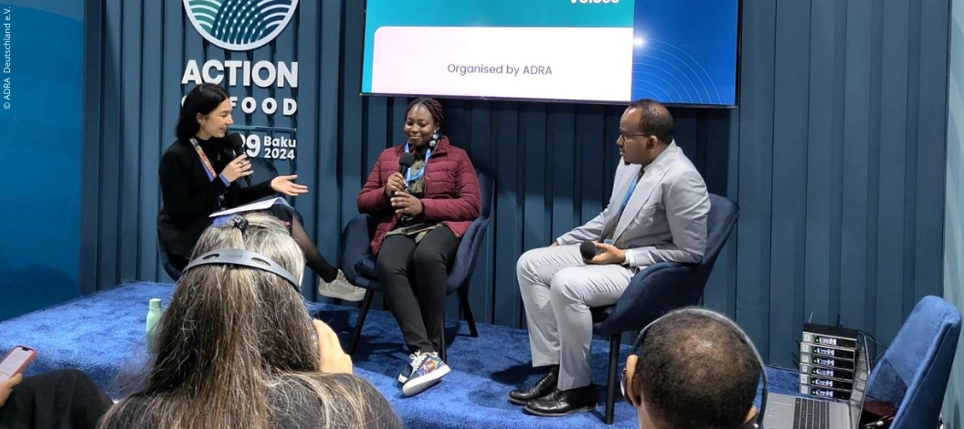 Carina Rolly, ADRA-Referentin, spricht auf der COP29 in Baku vor großem Publikum, mit zwei weiteren Personen auf der Bühne.