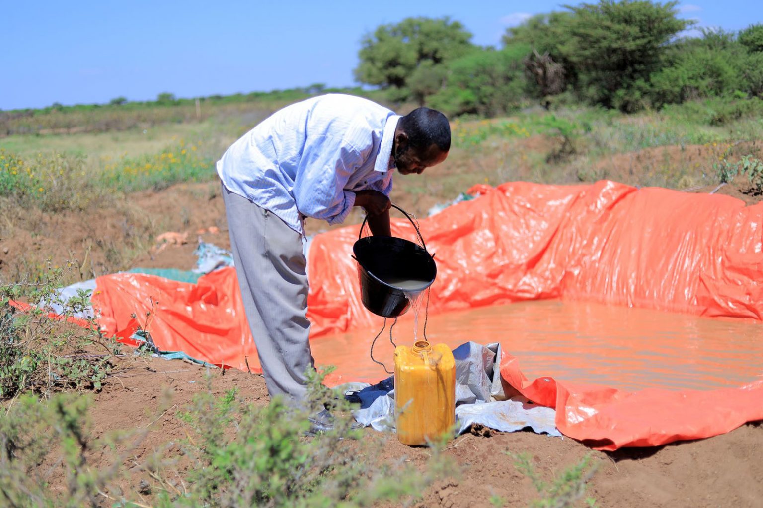 Mann schöpft Wasser aus einem improvisierten Wasserreservoir in einen gelben Kanister in Somalia.