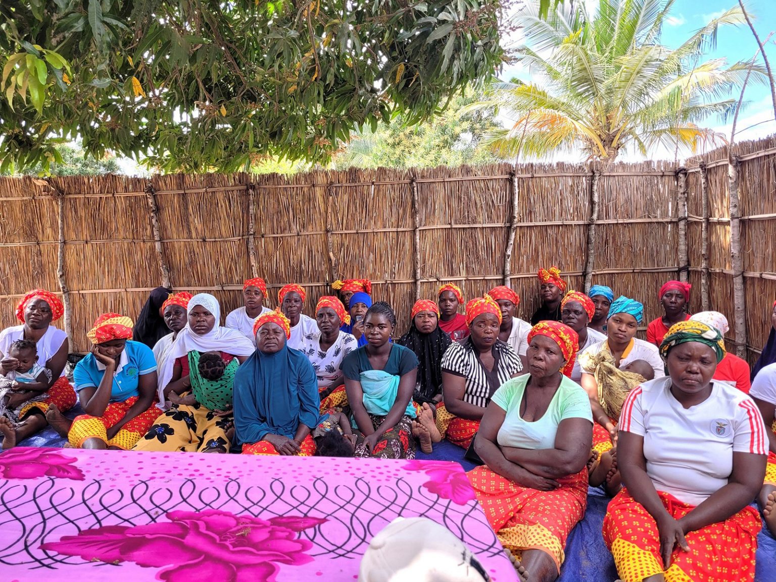 Gruppe von etwa 25 Frauen mit bunten Kopftüchern sitzt in einem offenen Versammlungsraum aus Holz.