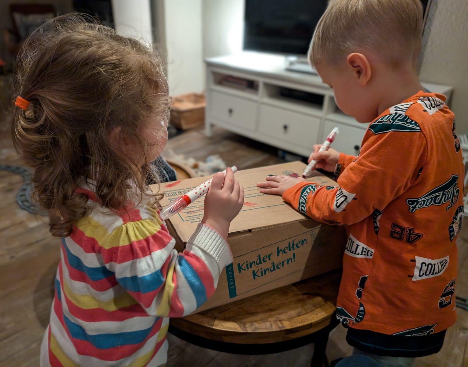 Anni (2 Jahre) und Emil (4 Jahre) verzieren das Paket, das Sie für die „Aktion Kinder helfen Kindern!“ gepackt haben. (Foto: Angela Völker)