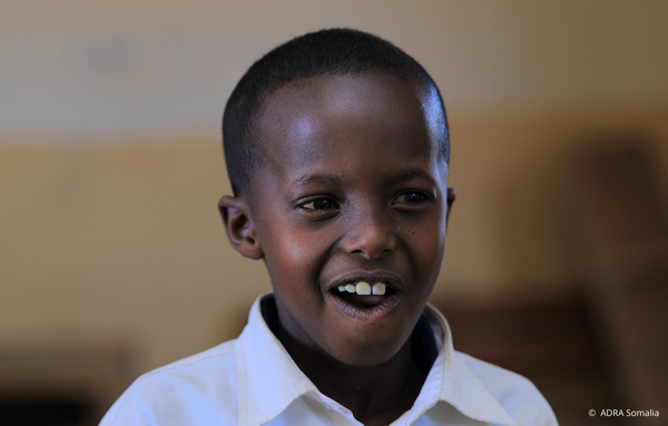 Ein somalischer Junge in Schuluniform lächelt fröhlich in die Kamera. Das Bild symbolisiert die Hoffnung und Freude, die durch die Bildungsprojekte von ADRA und Save the Children im Krisengebiet Somalia vermittelt werden.