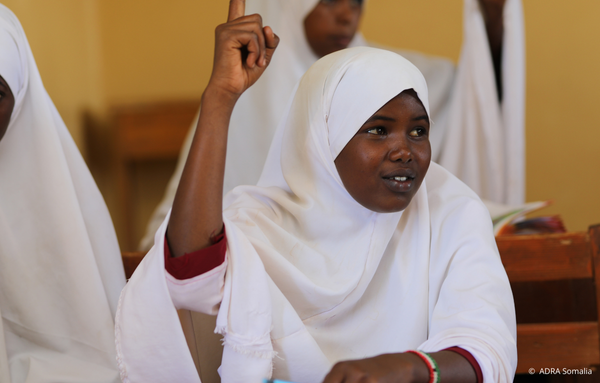 Ein somalisches Mädchen in Schuluniform hebt die Hand im Klassenzimmer. Dank der Unterstützung von ADRA und Save the Children kann sie wieder am Unterricht teilnehmen und eine bessere Bildung erhalten.