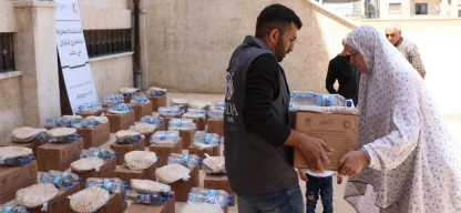 ADRA-Helfer überreicht syrischer Frau Hilfspaket mit Wasser und Fladenbrot – umgeben von weiteren gepackten Kartons