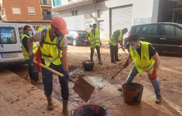 ADRA-Helfer räumen mit Schaufeln Schlamm und Trümmer von den Straßen in einer von der Flut betroffenen Stadt in Valencia.