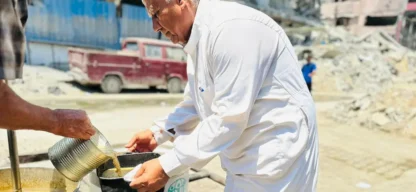 Gaza Nothilfe - Älterer Mann erhält Suppe aus großem Topf mit ADRA-Logo – im Hintergrund Trümmer und zerstörte Gebäude