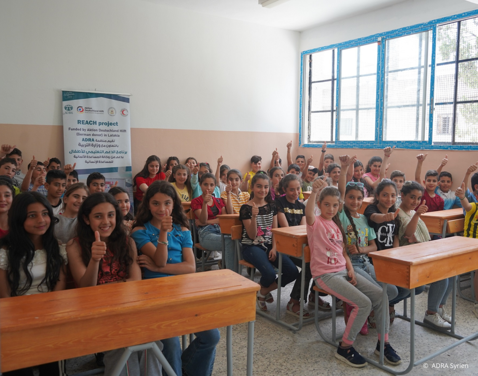 Gruppe syrischer Kinder und Jugendlicher im Klassenzimmer lächelt und zeigt Daumen hoch – ADRA-Bildungsprojekte nach dem Erdbeben