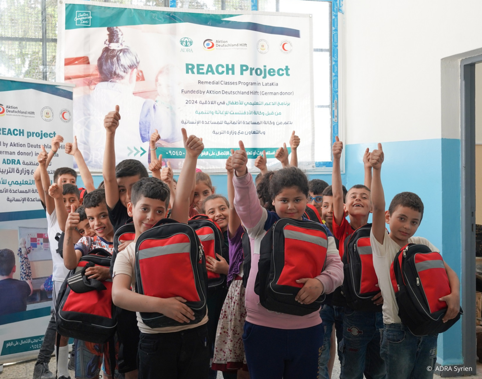 Syrische Kinder mit roten Schulranzen im Klassenzimmer zeigen Daumen hoch – ADRA-Bildungsprogramm nach dem Erdbeben