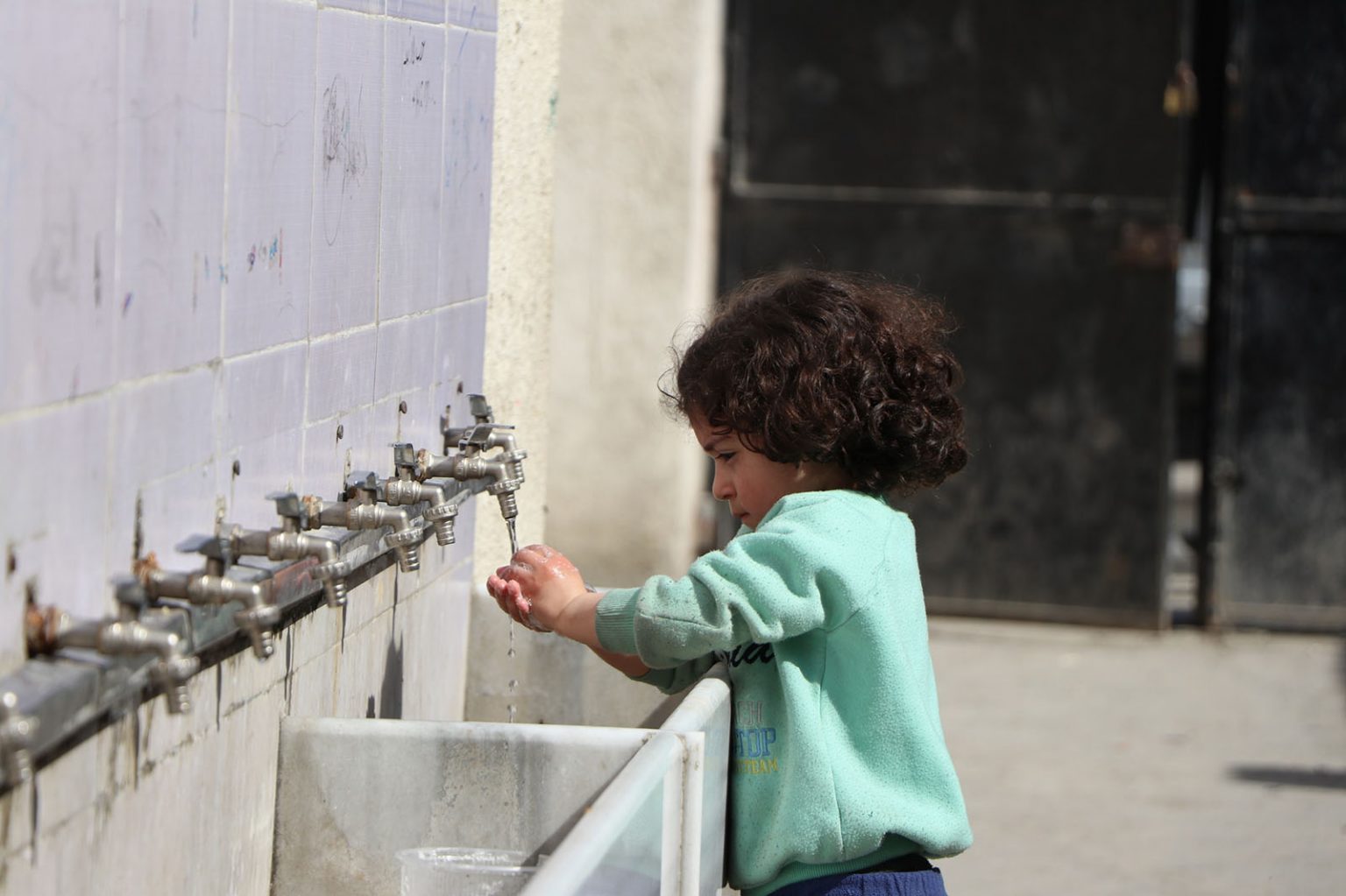 Syrisches Mädchen wäscht sich an Wasserhähnen die Hände – ADRA-Projekte stellen Wasserinfrastruktur wieder her.