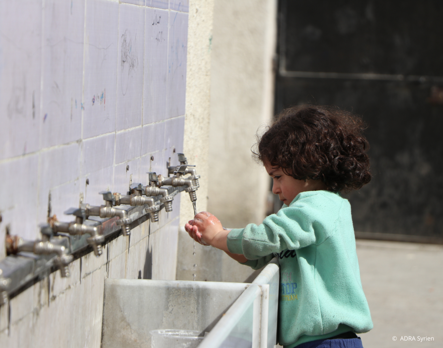 Syrisches Mädchen wäscht sich an Wasserhähnen die Hände – unterstützt durch ADRA-Projekte zur Wiederherstellung der Wasserinfrastruktur