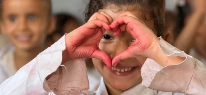 Mädchen in jemenitischer Schulklasse formt mit rot bemalten Händen ein Herz vor dem Gesicht und blickt hindurch