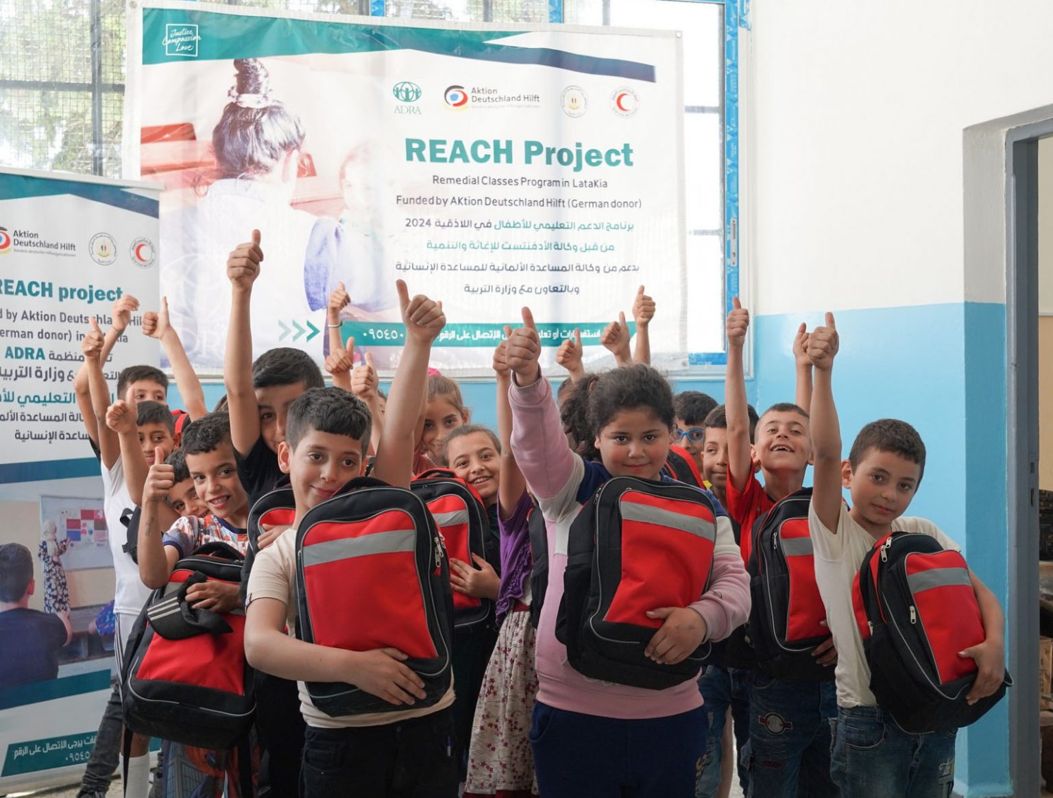 Syrische Kinder mit roten Schulranzen im Klassenzimmer zeigen Daumen hoch – ADRA-Bildungsprogramm nach dem Erdbeben