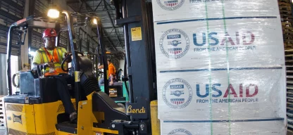 Ein Gabelstaplerfahrer transportiert Hilfsgüter mit dem USAID-Logo in einem Lagerhaus.