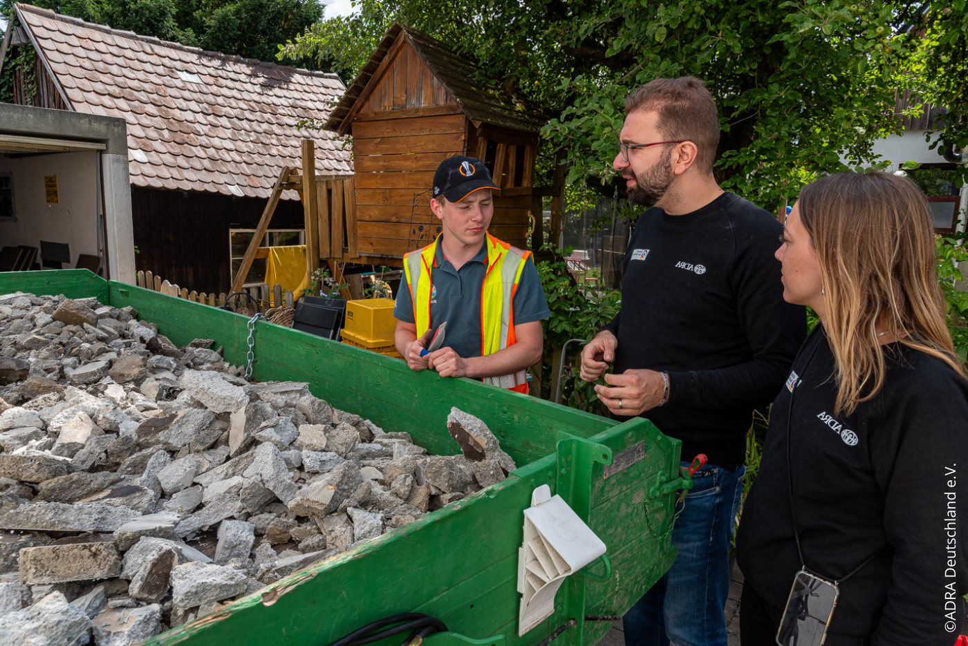 ADRA-Mitarbeitende sprechen mit einem Einsatzleiter neben einem Container mit Trümmern.