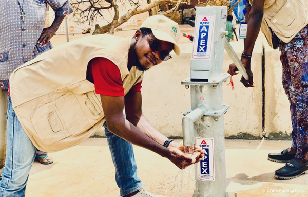 Ein Mann aus Burkina Faso wäscht sich lächelnd die Hände an einem Brunnen und blickt in die Kamera.