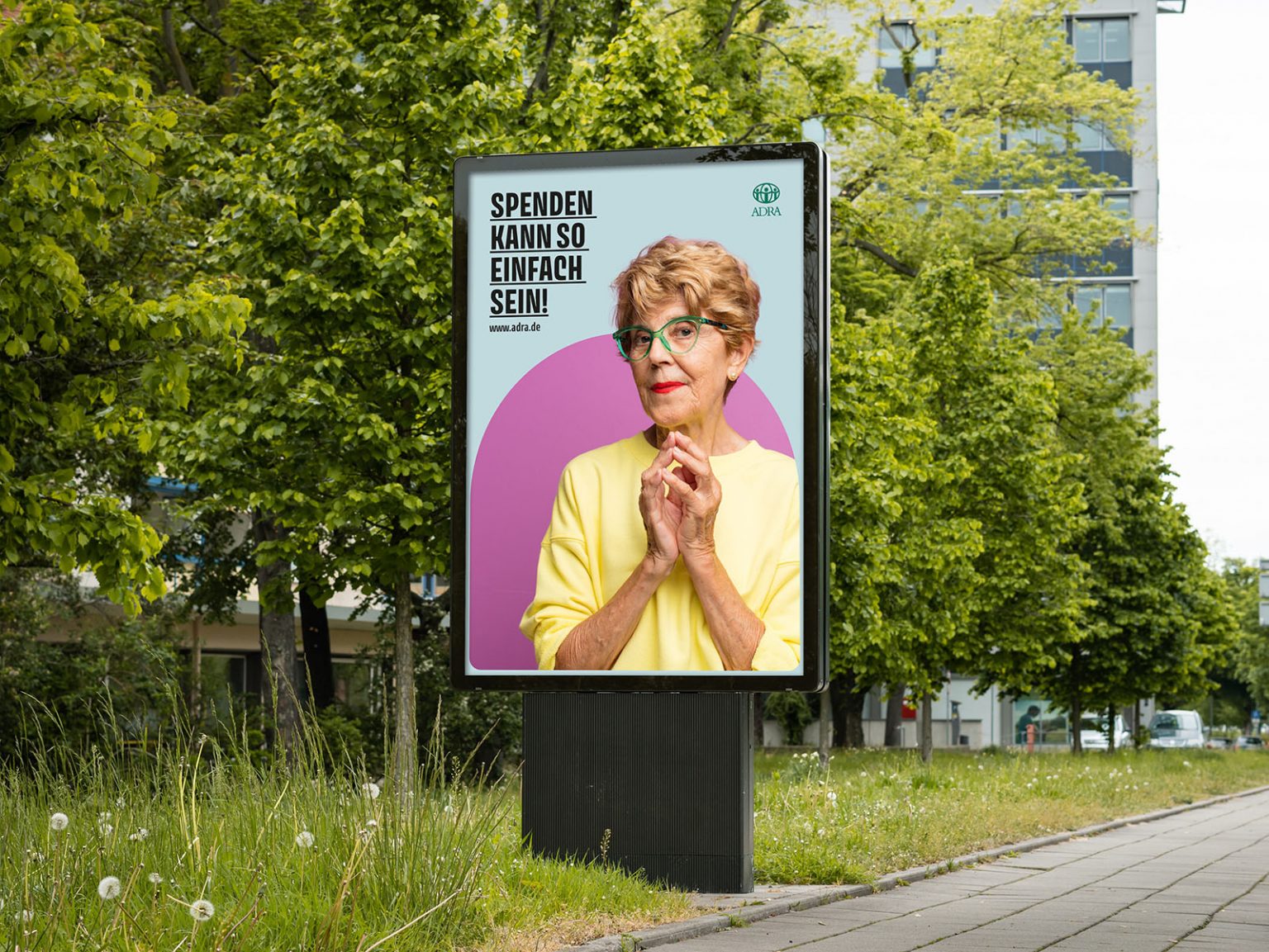 Großplakat mit älterer Frau in gelbem Pullover und Brille, Text „Spenden kann so einfach sein!“ – ADRA-Kampagne (Illustration: Peter Paul and Mary Werbeagentur GmbH & Co. KG)