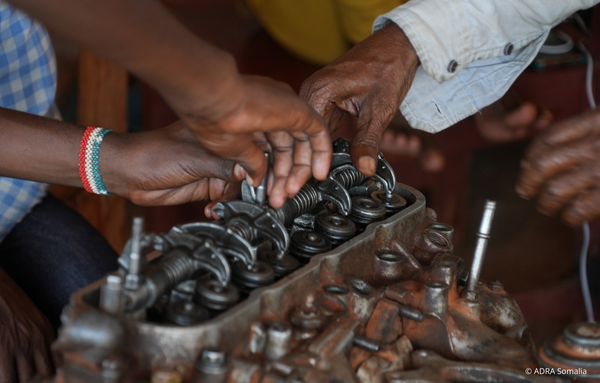 Nahaufnahme von Händen, die im ADRA-IMPACT-Projekt in Somalia an einem Motor arbeiten – praktische Ausbildung in grüner Mechanik.