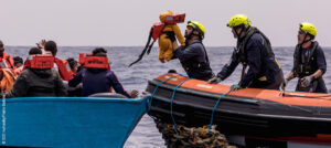 Boot mit Geflüchteten neben Rettungsboot von SOS Humanity – Kleinkind wird ins Rettungsboot gehoben. © SOS Humanity/Pietro Bertora