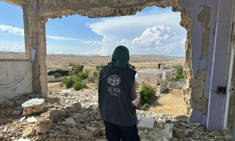 ADRA-Mitarbeiterin steht im Freien vor zerstörten Gebäuden in Syrien nach dem Erdbeben 2023. | ©ADRA Syrien
