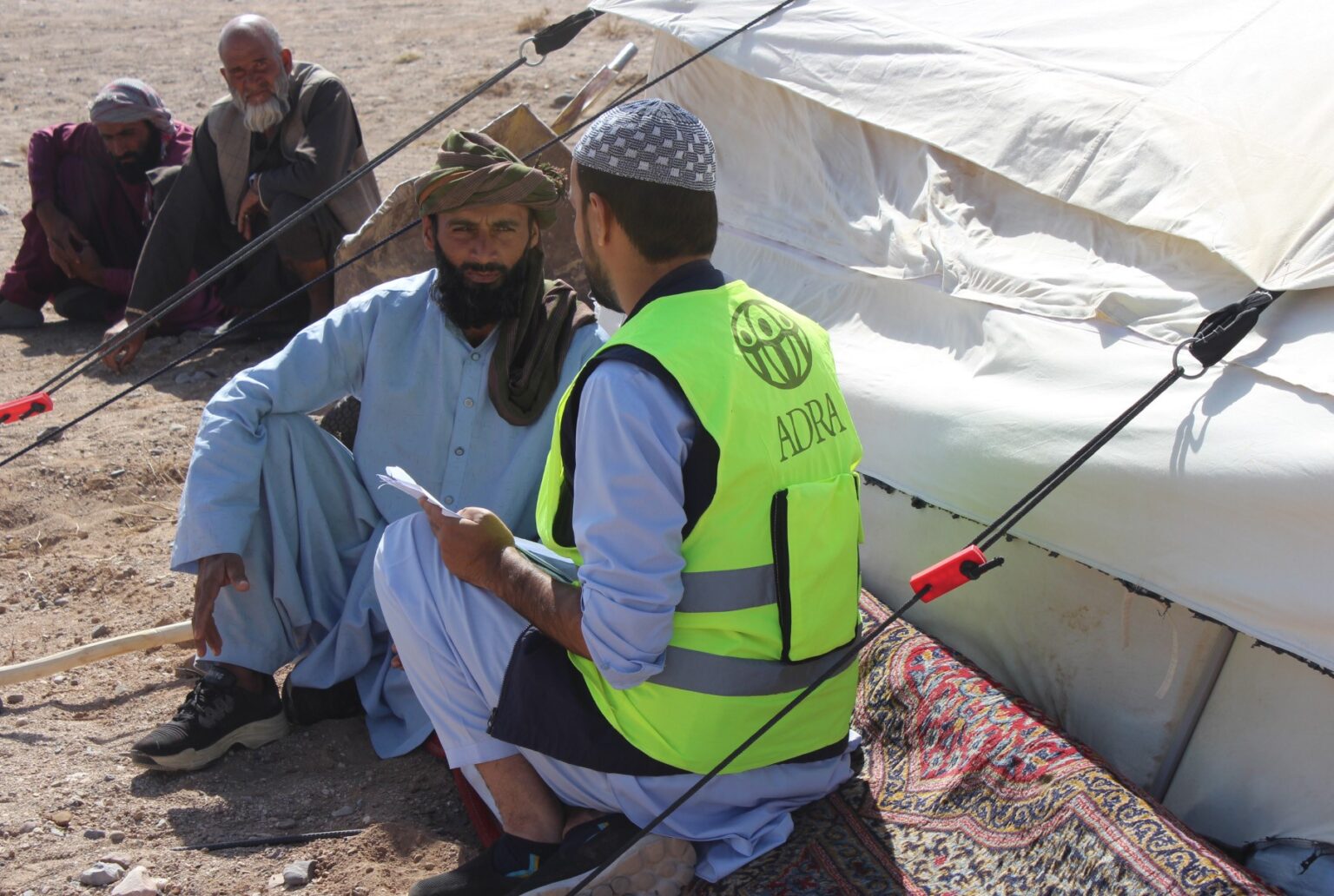 ADRA-Mitarbeiter im Gespräch mit einem vom Erdbebenbetroffenen Anwohner in Afghanistan vor einem Notzelt, Symbolbild für humanitäre Nothilfe
