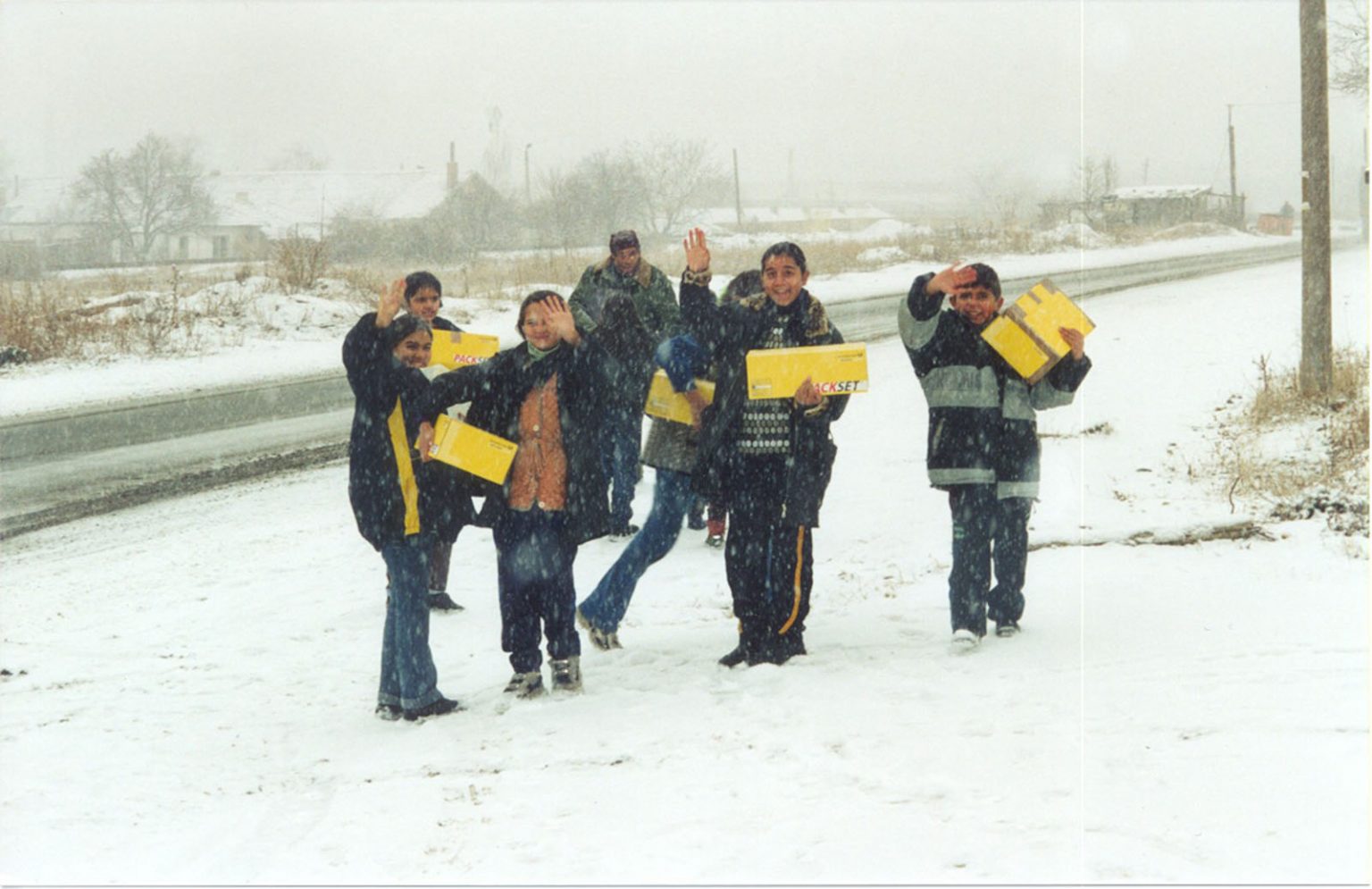 Kinder in Bulgarien winken im Schneefall und tragen gelbe Hilfspakete (ADRA Deutschland e.V., 2002).