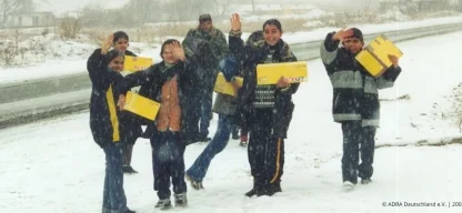 Kinder in Bulgarien winken im Schneefall und tragen gelbe Hilfspakete (ADRA Deutschland e.V., 2002).