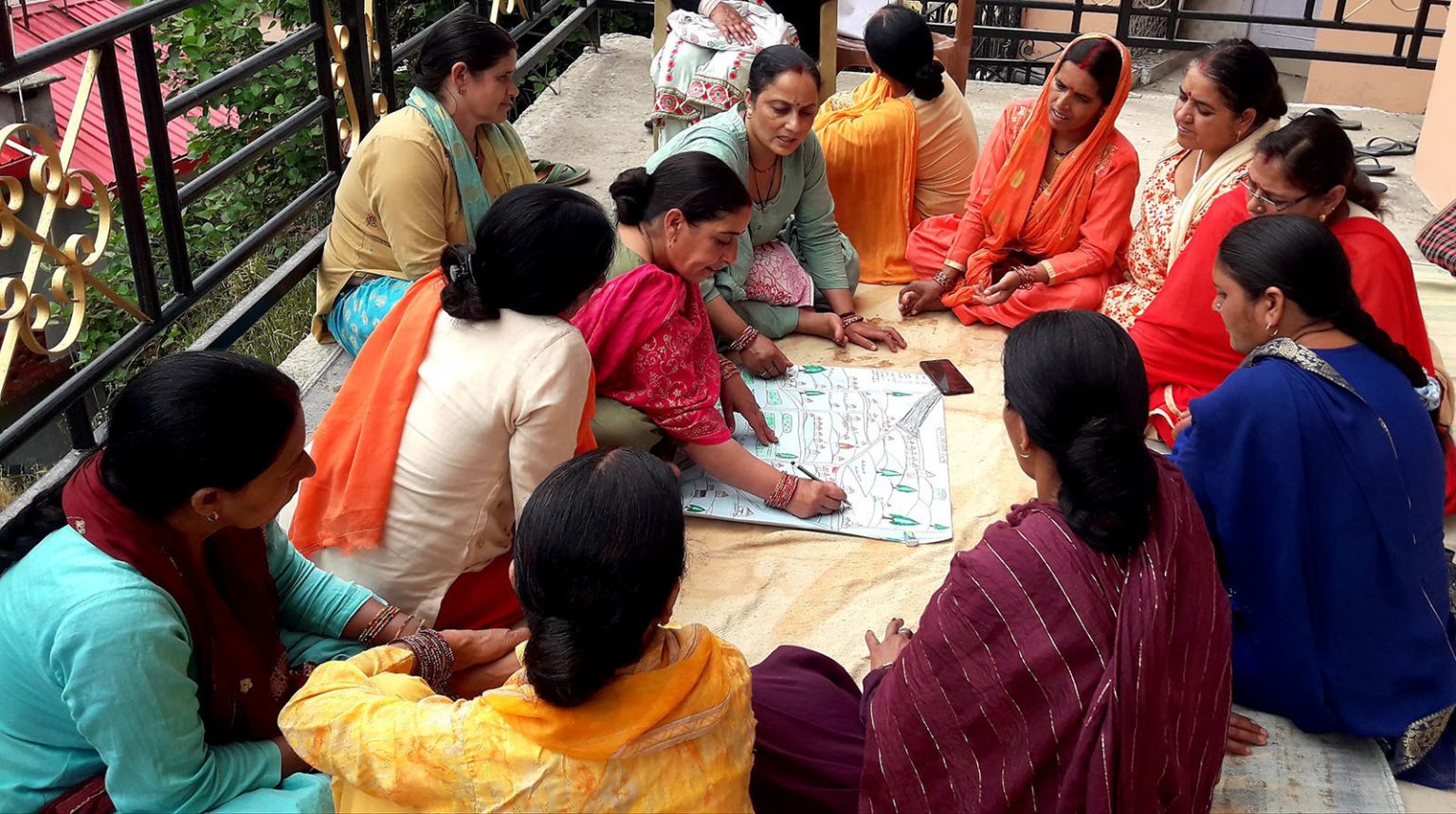 Frauen in Himachal Pradesh, Indien, sitzen gemeinsam im Kreis und besprechen einen Plan. ADRA unterstützt sie dabei, nach Überschwemmungen ihre Lebensgrundlagen wiederherzustellen und durch lokale Notfallpläne besser auf künftige Katastrophen vorbereitet zu sein.