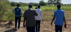 Feldarbeiter und ADRA-Mitarbeiter gehen über ein Ackerfeld in Somalia, um landwirtschaftliche Projekte und Erntebedingungen zu begutachten.