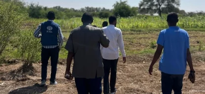 Feldarbeiter und ADRA-Mitarbeiter gehen über ein Ackerfeld in Somalia, um landwirtschaftliche Projekte und Erntebedingungen zu begutachten.