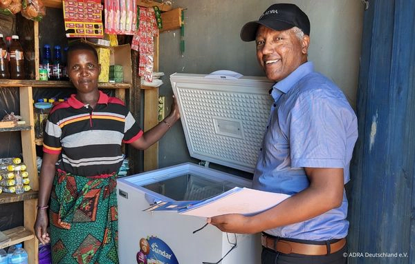 Eine Kleinunternehmerin in Tansania erhält mit Unterstützung von ADRA eine solarbetriebene Kühltruhe für ihren Laden – grüne Technologie fördert nachhaltige wirtschaftliche Entwicklung.