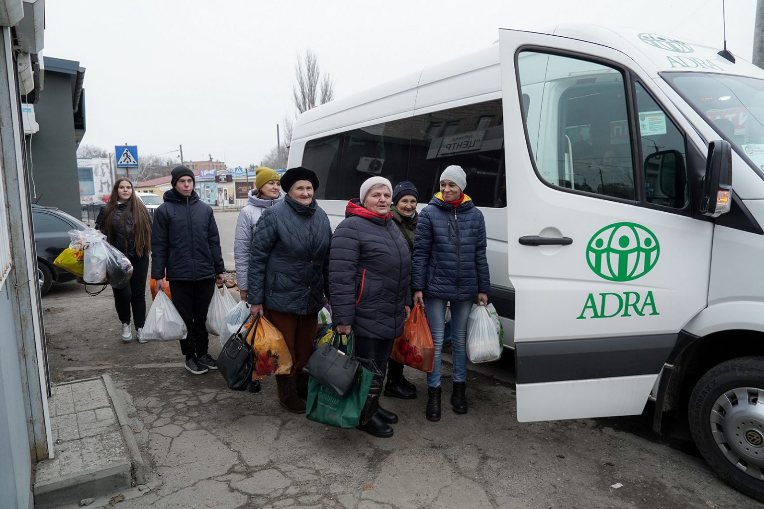 Mehrere Frauen stehen mit Einkaufstaschen neben einem ADRA-Bus in der Ukraine und erhalten Hilfsgüter.