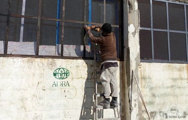 Arbeiter repariert Fenster eines beschädigten Schulgebäudes im Rahmen der ADRA-Wiederaufbauarbeiten in Syrien.