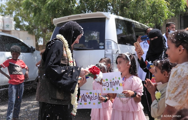 Mehrere Kinder im Jemen begrüßen Verena, Teamleiterin Asien-Pazifik mit Blumen und selbstgemalten Schildern, während Konfetti in der Luft liegt.