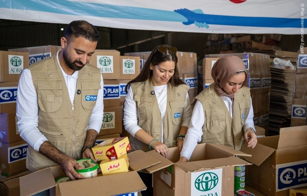 Drei Helfer packen Hilfspakete mit Lebensmitteln und Kleidung für vertriebene Familien in Gaza im Rahmen der Winterhilfe.