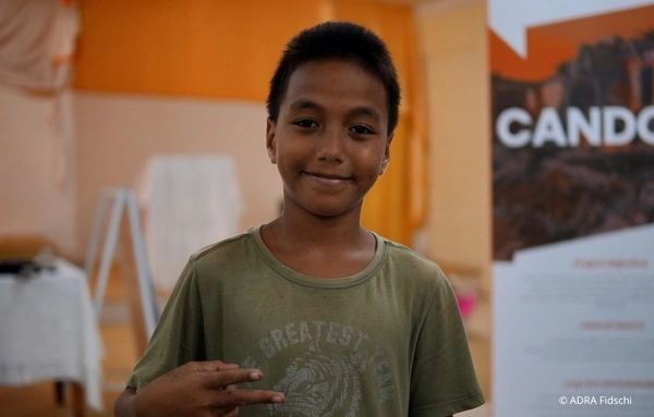 Junge auf Fidschi steht vor einem ADRA-Projektbanner und profitiert von Maßnahmen zur nachhaltigen Katastrophenvorsorge