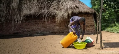Eine Frau nutzt Wasser aus einem gelben Kanister für den Haushalt vor ihrem Haus in der Demokratischen Republik Kongo.