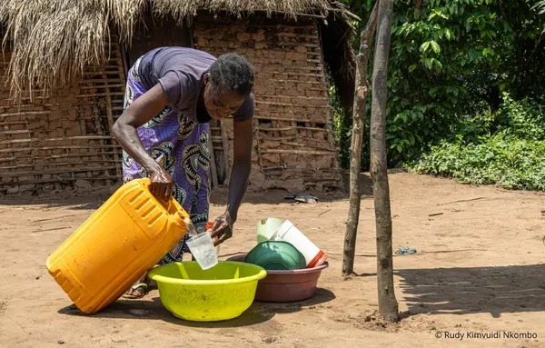 Eine Frau nutzt Wasser aus einem gelben Kanister für den Haushalt vor ihrem Haus in der Demokratischen Republik Kongo.