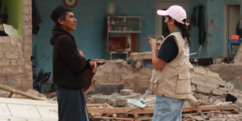 Eine ADRA-Mitarbeiterin aus Indonesien steht mit einem vom erdbebenbetroffenen Bewohner vor den Trümmern eines Hauses