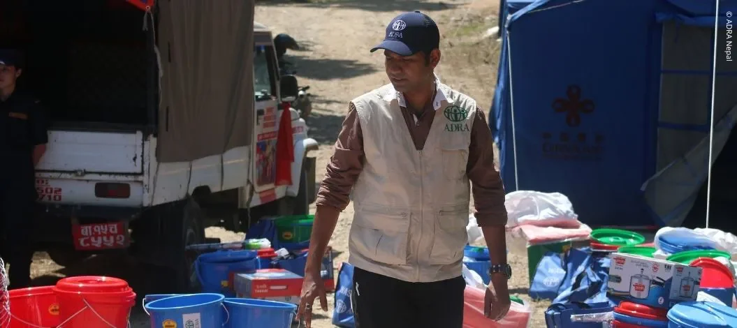 ADRA-Mitarbeiter steht zwischen Eimern, Taschen und weiteren Hilfsgütern in einem provisorischen Versorgungsbereich in Nepal
